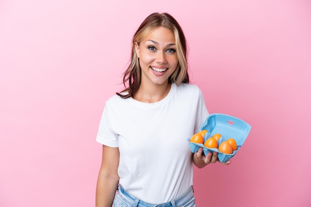 Young Russian woman holding eggs isolated on pink background with surprise facial expression