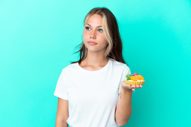 Young Russian woman holding a fruit sweet isolated on blue background looking to the side