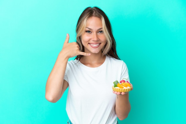 Foto giovane donna russa che tiene un dolce di frutta isolato su sfondo blu che fa il gesto del telefono. richiamami segno