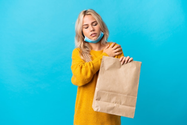 Young Russian woman holding a grocery shopping bag isolated on blue background suffering from pain in shoulder for having made an effort