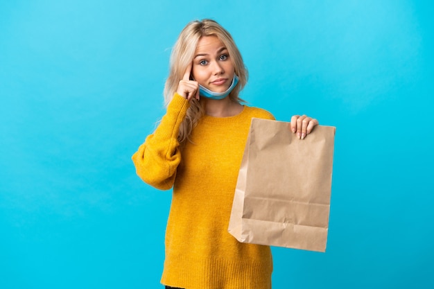 アイデアを考えて青に分離された食料品の買い物袋を保持している若いロシアの女性