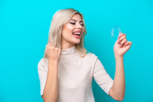 Young Russian woman holding invisaging isolated on blue background celebrating a victory