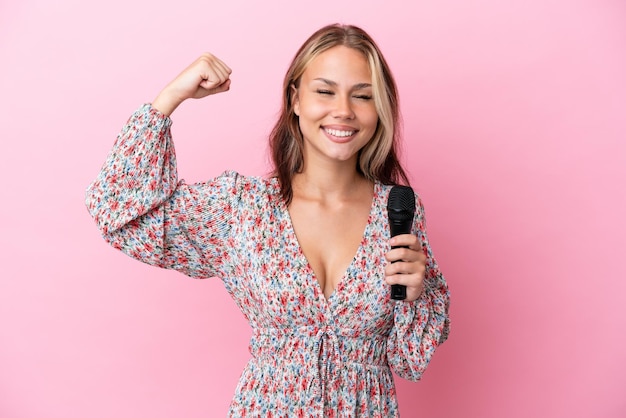 Young Russian woman holding a microphone isolated on pink background doing strong gesture