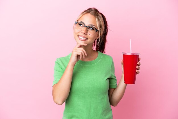 Молодая русская женщина держит прохладительные напитки на розовом фоне и смотрит вверх