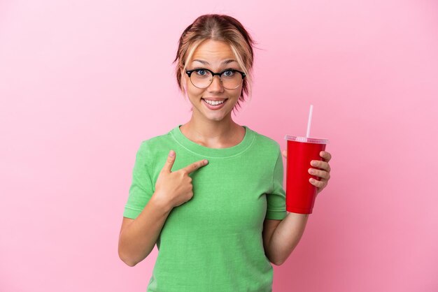 Young Russian woman holding a refreshment isolated on pink background with surprise facial expression