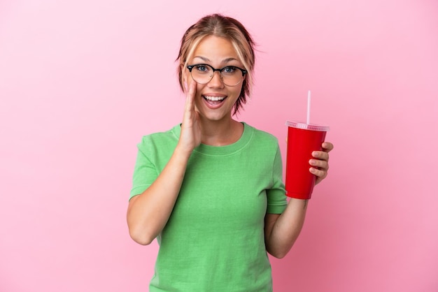 Young Russian woman holding a refreshment isolated on pink background with surprise and shocked facial expression