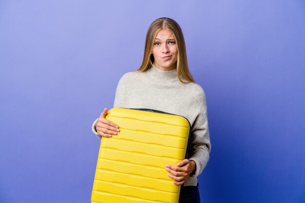 Young russian woman holding suitcase to travel unhappy looking in camera with sarcastic expression