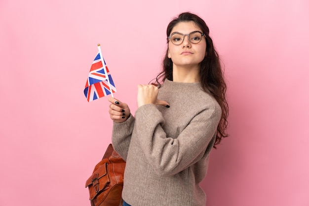 Photo young russian woman holding an united kingdom flag isolated on pink background proud and self-satisfied