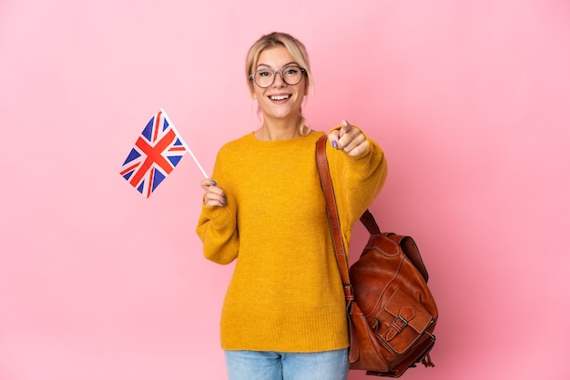 Young Russian woman holding an United Kingdom flag isolated on pink surprised and pointing front