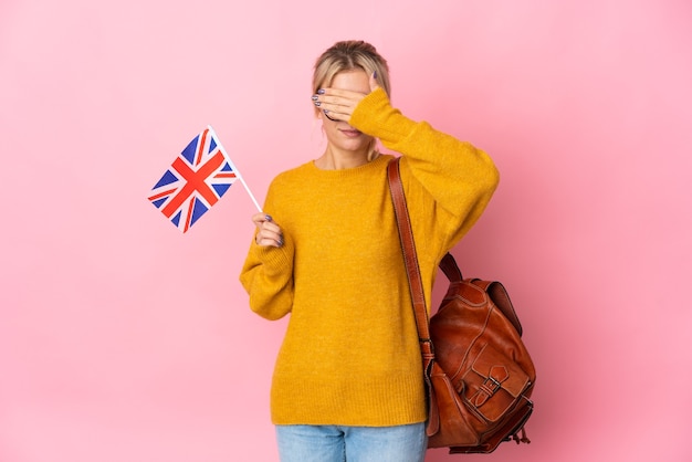 Young Russian woman holding an United Kingdom flag isolated on pink wall covering eyes by hands. Do not want to see something