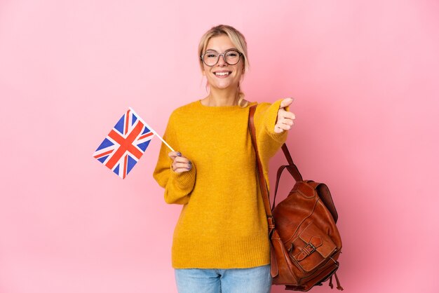 Young Russian woman holding an United Kingdom flag isolated on pink wall shaking hands for closing a good deal