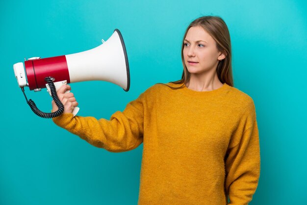 強調された表情でメガホンを保持している青い背景に分離された若いロシアの女性