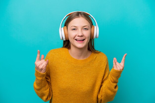 Young russian woman isolated on blue background listening music\
making rock gesture