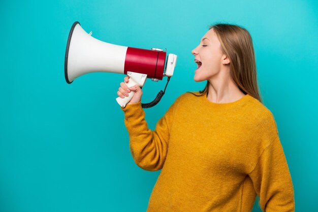 Young Russian woman isolated on blue background shouting through a megaphone to announce something in lateral position