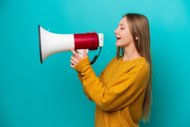 Young Russian woman isolated on blue background shouting through a megaphone to announce something in lateral position