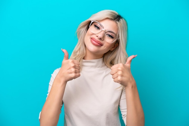 Young Russian woman isolated on blue background With glasses and with thumb up