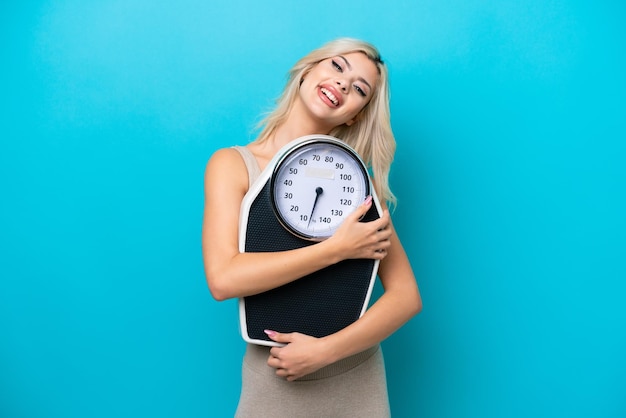 Young Russian woman isolated on blue background with weighing machine