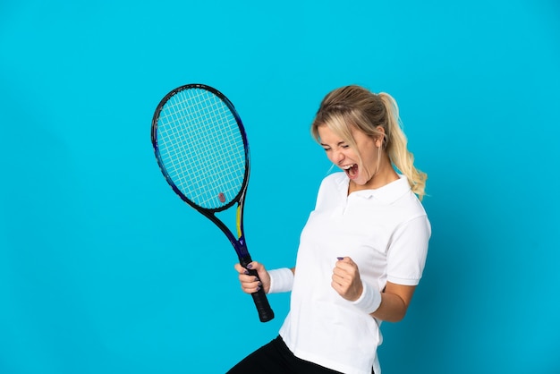 Молодая россиянка изолирована на синей стене играет в теннис и празднует победу