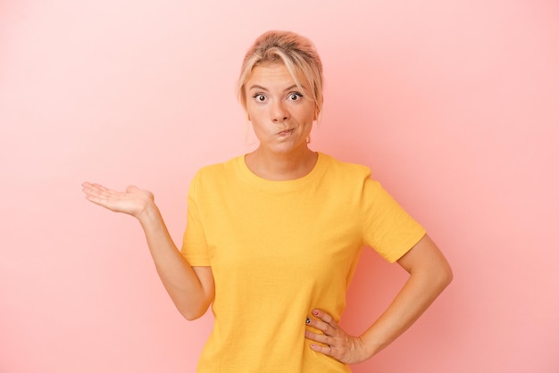 Young Russian woman isolated on pink background showing a copy space on a palm and holding another hand on waist