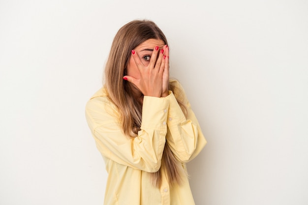 Young Russian woman isolated on white background blink through fingers frightened and nervous.