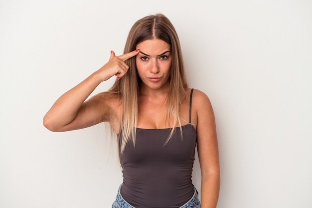 Foto giovane donna russa isolata su sfondo bianco che punta il tempio con il dito, pensando, focalizzata su un compito.