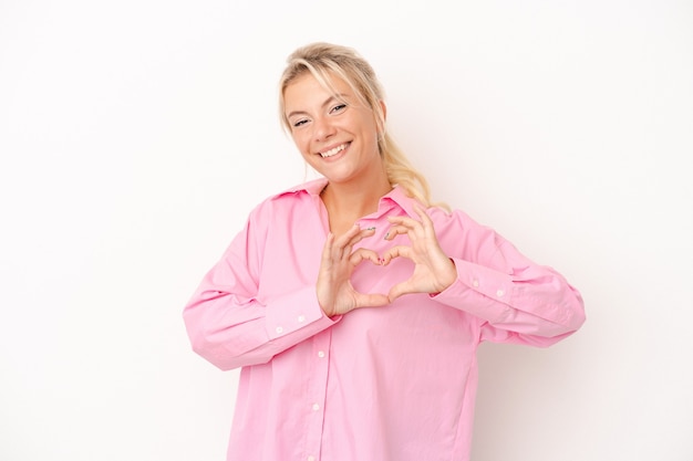 Young Russian woman isolated on white background smiling and showing a heart shape with hands.