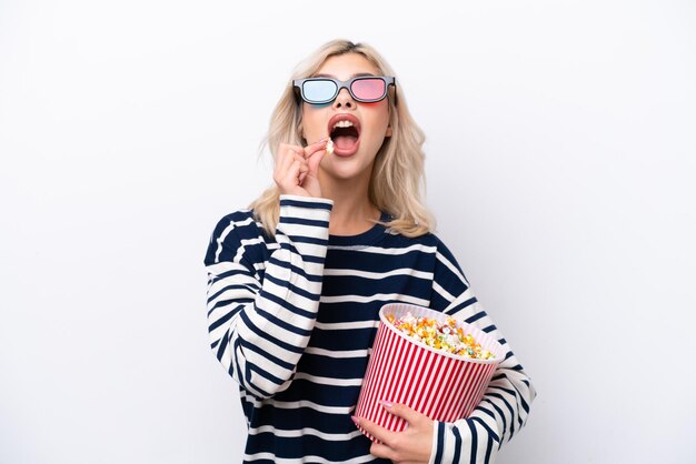 Young Russian woman isolated on white background with 3d glasses and holding a big bucket of popcorns