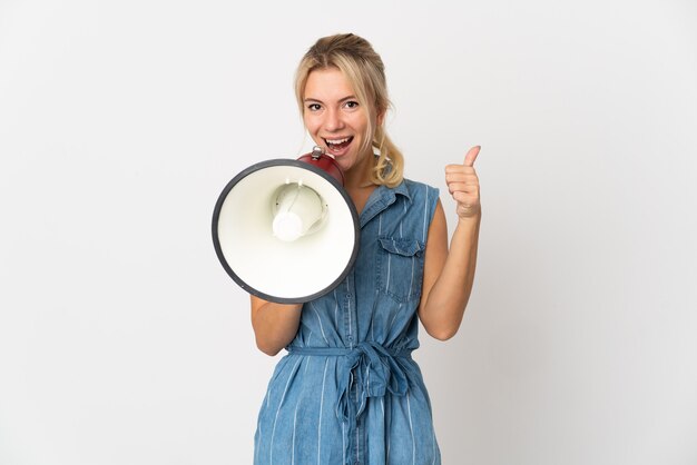 Young Russian woman isolated on white wall shouting through a megaphone to announce something and with thumb up