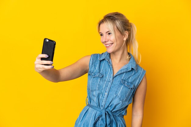 Young Russian woman isolated on yellow background making a selfie with mobile phone