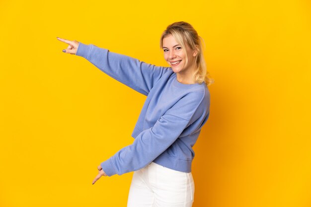 Young Russian woman isolated on yellow background pointing finger to the side and presenting a product