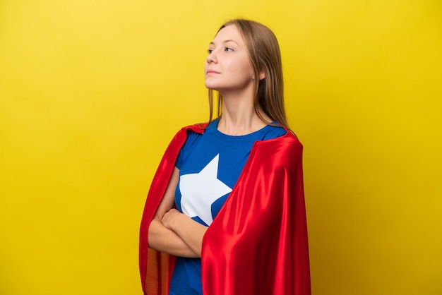 Young Russian woman isolated on yellow background in superhero costume with arms crossed