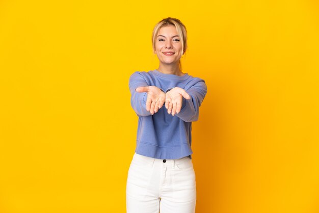 광고를 삽입하려면 손바닥에 가상 copyspace를 들고 노란색 벽에 고립 된 젊은 러시아 여자