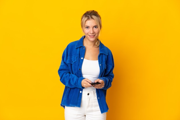 Young Russian woman isolated on yellow wall sending a message with the mobile