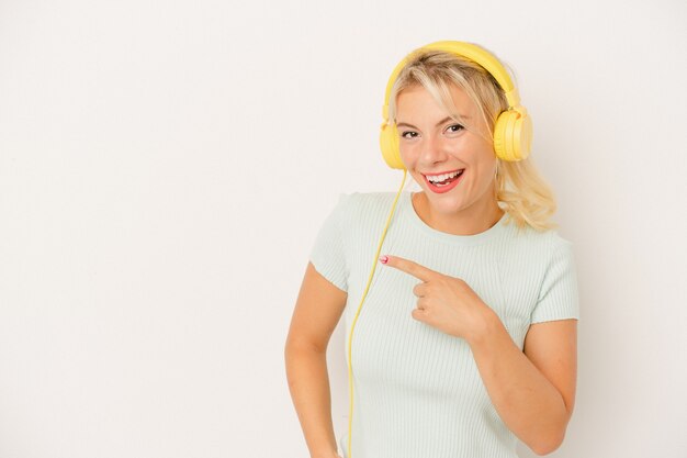 Foto giovane donna russa che ascolta la musica isolata su fondo bianco che sorride e che indica da parte, mostrando qualcosa nello spazio vuoto.