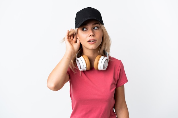 Young Russian woman listening music isolated on white wall listening to something by putting hand on the ear