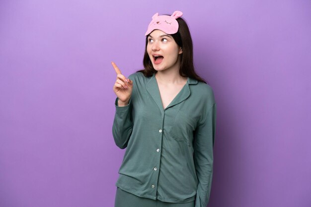 指を持ち上げながら解決策を実現することを意図して紫色の背景に分離されたパジャマの若いロシアの女性