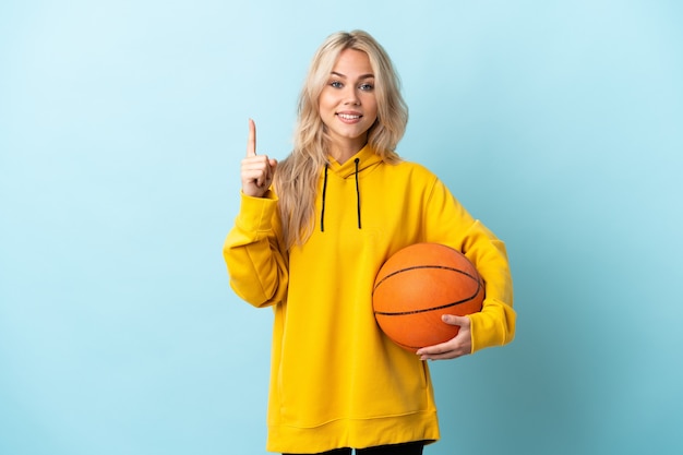 Young Russian woman playing basketball isolated on blue wall pointing up a great idea