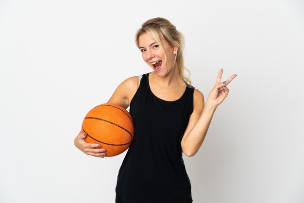 白い笑顔と勝利のサインを示す上で隔離のバスケットボールをしている若いロシアの女性
