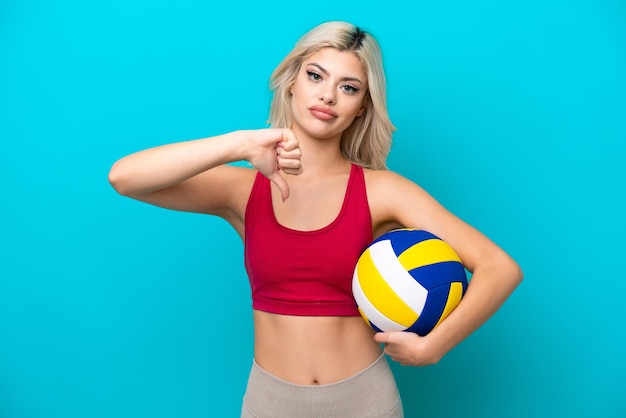 Young Russian woman playing volleyball isolated on blue background showing thumb down with negative expression