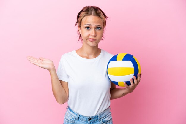 Young Russian woman playing volleyball isolated on pink background having doubts while raising hands