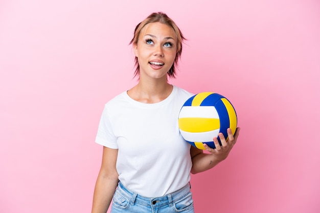 Молодая русская женщина, играющая в волейбол на розовом фоне, смотрит вверх и с удивленным выражением лица