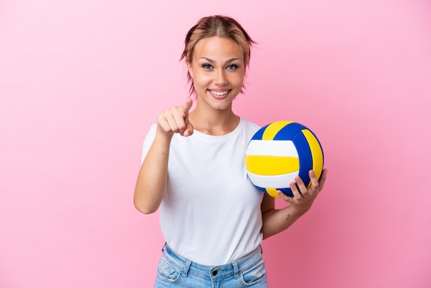 Young Russian woman playing volleyball isolated on pink background surprised and pointing front