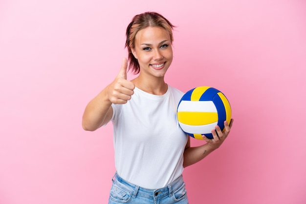 Young Russian woman playing volleyball isolated on pink background with thumbs up because something good has happened