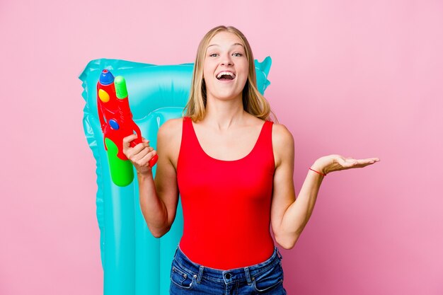 Young russian woman playing with a water gun with an air mattress celebrating a victory or success, he is surprised and shocked.