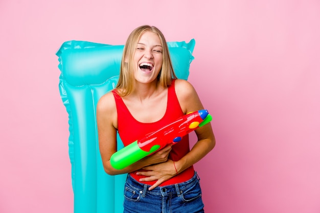 Young russian woman playing with a water gun with an air mattress laughs happily and has fun keeping hands on stomach.