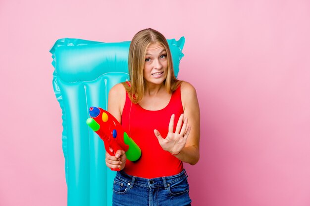 Young russian woman playing with a water gun with an air mattress rejecting someone showing a gesture of disgust.