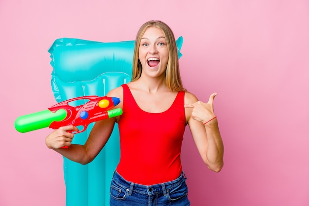 Young russian woman playing with a water gun with an air mattress surprised pointing with finger, smiling broadly