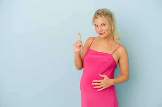 Young Russian woman pregnant isolated on blue background showing number one with finger.