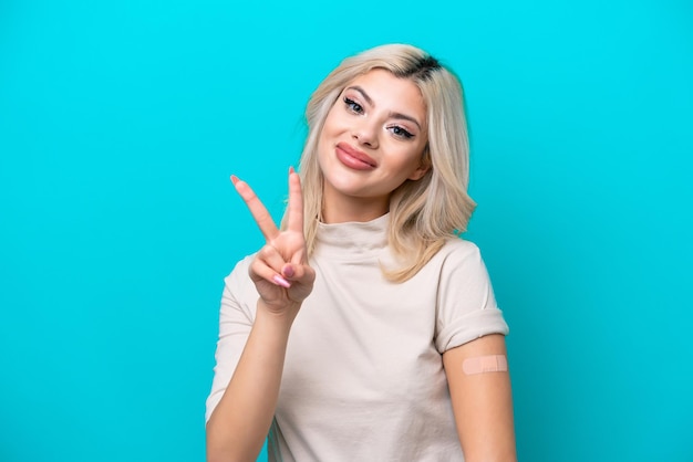 Young Russian woman wearing band aid isolated on blue background smiling and showing victory sign