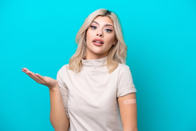 Young Russian woman wearing band aid isolated on blue background with shocked facial expression